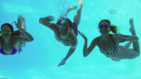 three friends diving into swimming pool and waving