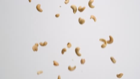 whole roasted and salted cashew nuts raining down and bouncing back into frame on white backdrop in slow motion