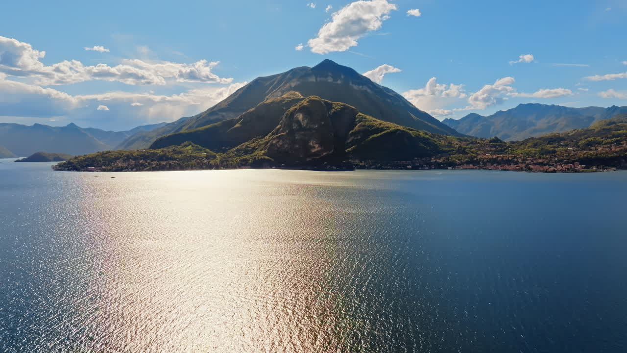 Aerial drone view of Lake Como, Italy surrounded by mountains with clouds on a blue sky