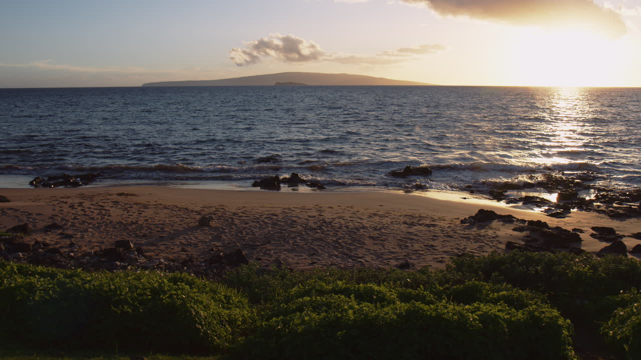 puesta de sol sobre el mar con olas salpicando en la orilla en wailea, maui, hawaii