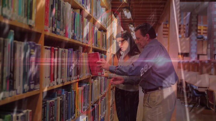 Colleghi che esaminano i dorsi dei libri nel corridoio di una biblioteca, mostrando sovrapposizioni di anni prima di prendere un libro rosso
