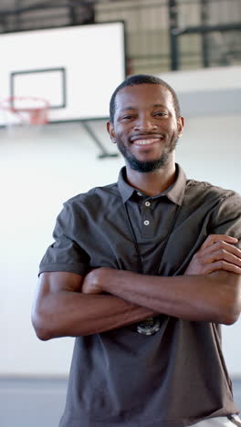 vertical video: standing with arms crossed, smiling basketball coach in gymnasium