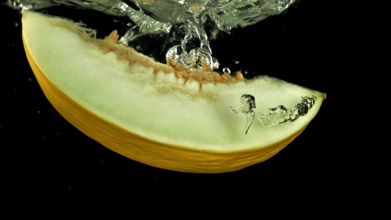 Fresh Melon Slice Submerging into Water with Bubbles on Black Background