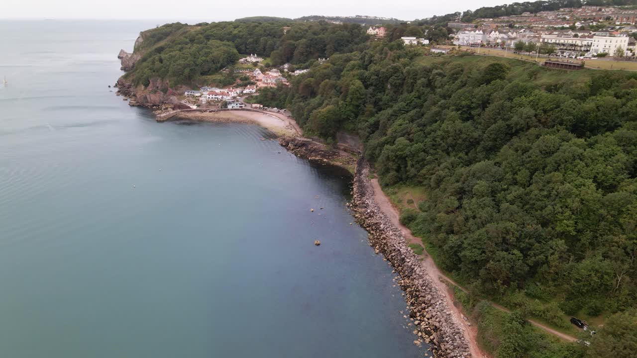 toma aérea en círculos de la famosa playa pedregosa de babbacombe con acantilados verdes y la ciudad de torquay en la cima de la montaña