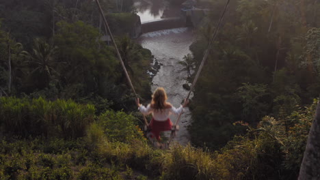 top view woman swinging over tropical rainforest at sunrise sitting on swing with view of river enjoying having fun on holiday travel freedom