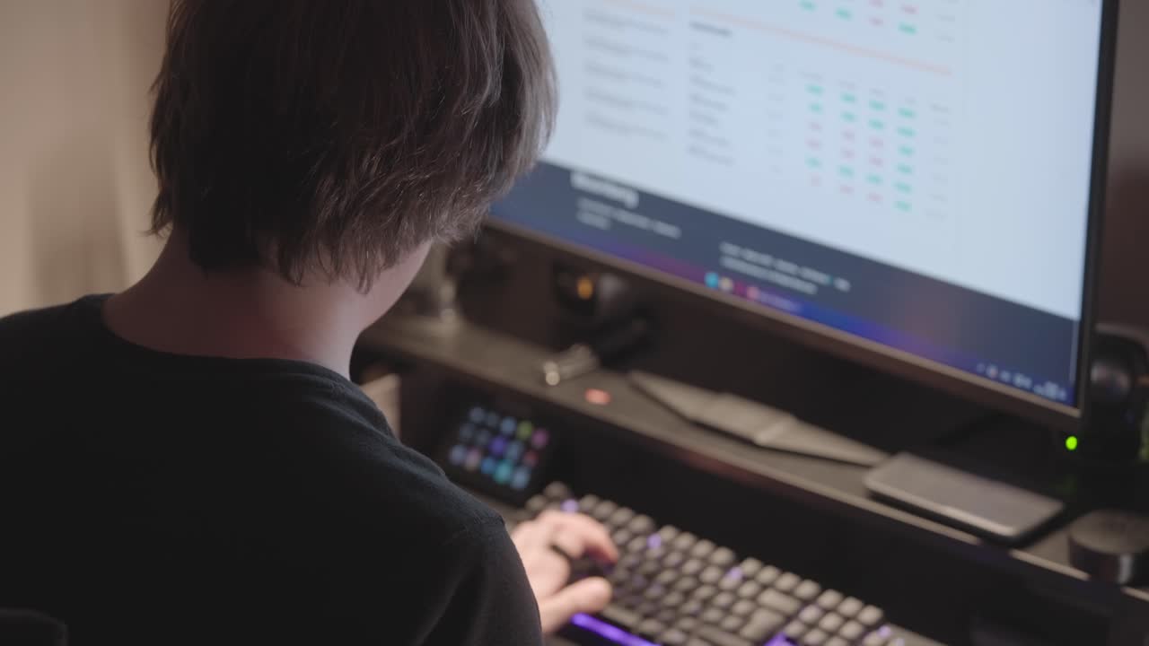Man at computer typing on keyboard by lamp light. Over-the-shoulder view in the evening