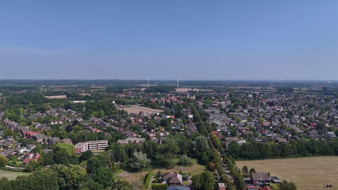 Suburb neighborhood with apartment blocks and row of homes in rural district of America. Sunny summer day near countryside. Aerial forward wide shot. Modern wind turbines producing energy from wind