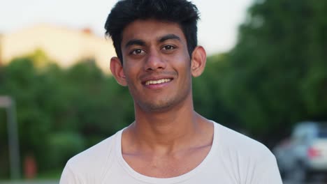 Young-Srilankan-man-smiles-and-nods-looking-at-camera-outdoor,-day
