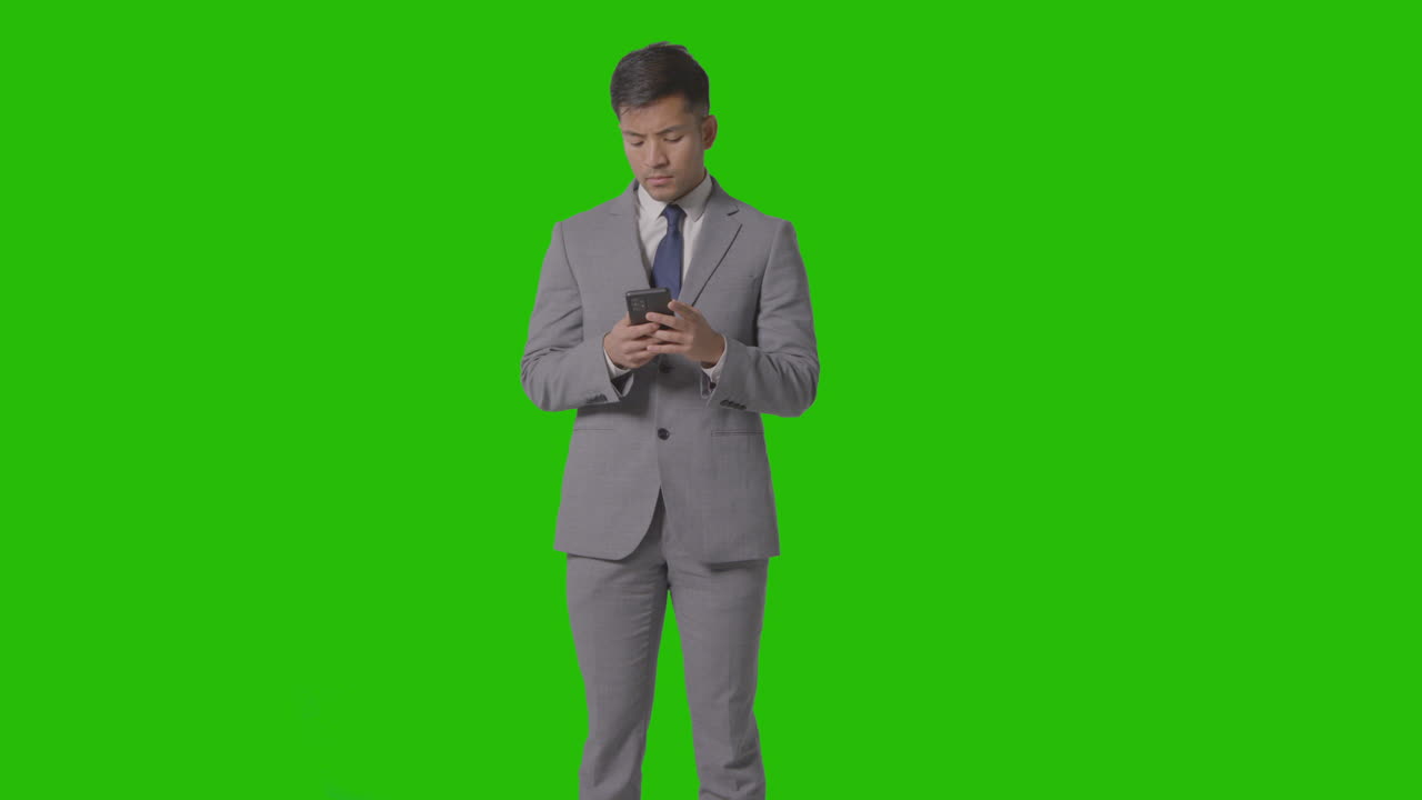 Three Quarter Length Studio Shot Of Businessman In Suit Looking At Mobile Phone Against Green Screen 2