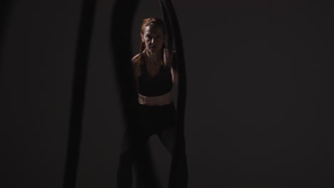 studio shot of mature woman wearing gym fitness clothing doing cardio exercise with battle ropes