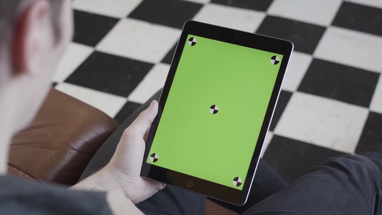Person holding a tablet with a green screen on a checkered floor