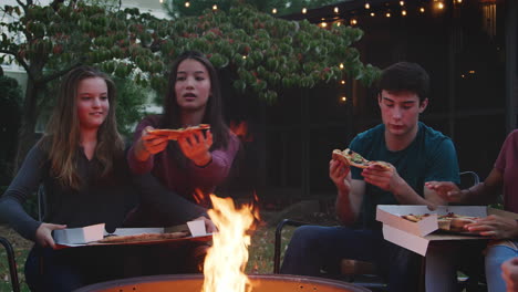 Teenage-friends-sit-round-a-firepit-eating-take-away-pizzas