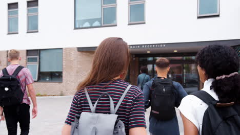 vista trasera de dos estudiantes de secundaria caminando juntos hacia el edificio de la universidad