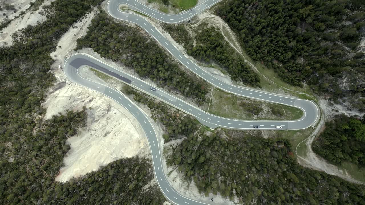 Tilt down aerial shot of cars driving sharp hairpin curves on alpine road