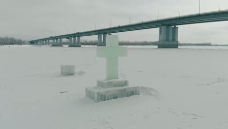 carved ice cross on white frozen river against bridge