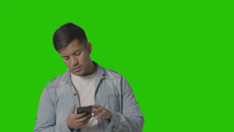 Studio-Shot-Of-Casually-Dressed-Young-Man-Messaging-On-Mobile-Phone-Against-Green-Screen-3