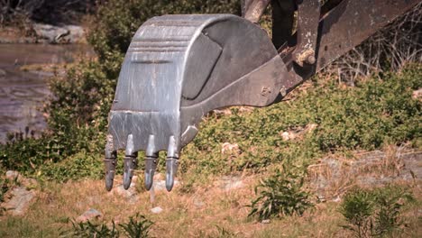 una gran cuchara de metal de una excavadora con dientes se mueve hacia los lados y se dobla en un pedazo de tierra