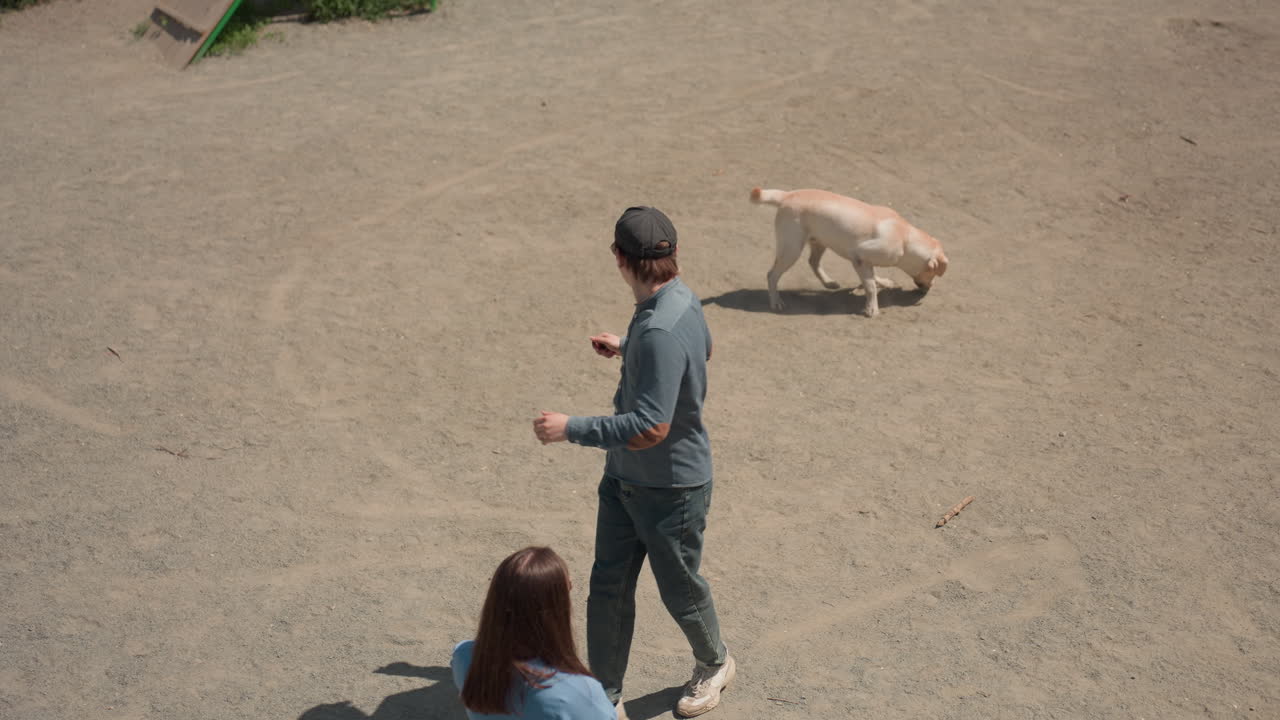맑은 하늘 아래, 넓은 흙밭을 강아지와 함께 빠르게 달리는 남자: 조깅하는 사람이 맑은 햇빛 아래 래브라도를 바로 뒤에 두고 광활한 훈련 공간을 활기차게 질주하고 있어요.