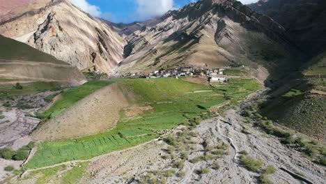 stunning-mountain-landscape-with-village-on-hill-full-of-lush-farmland-in-Pin-Valley-India,-aerial