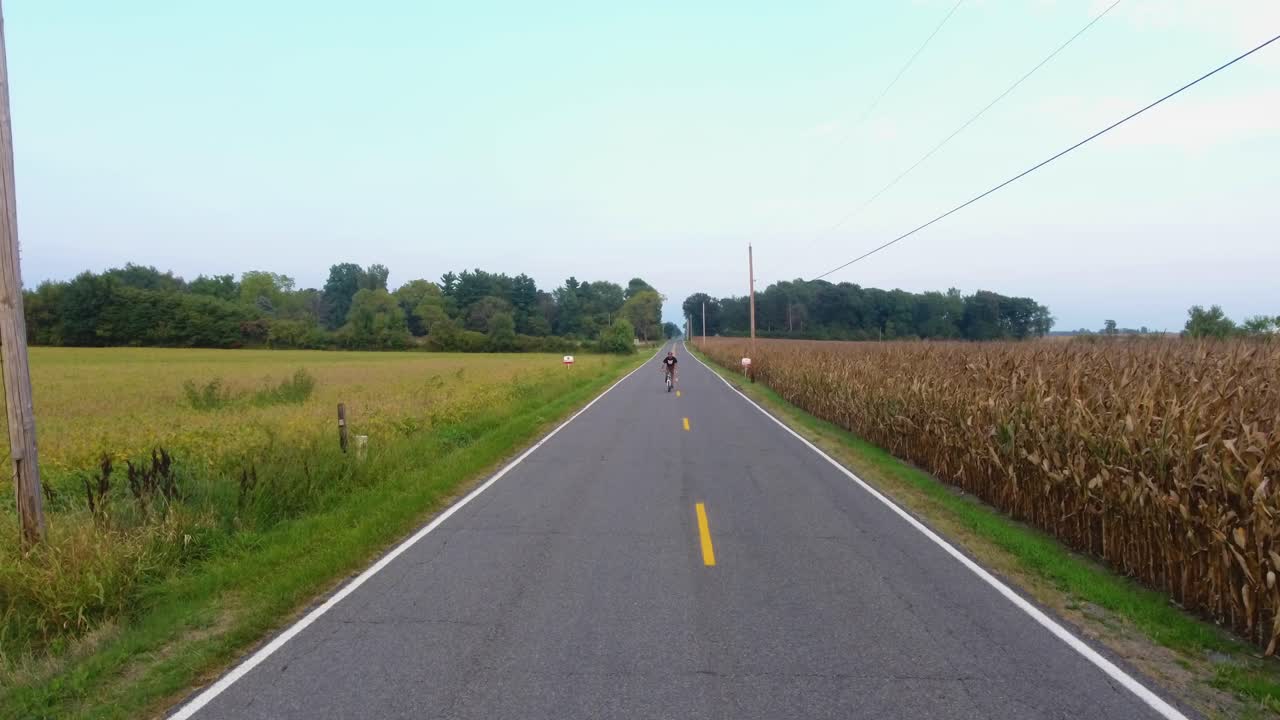 Aerial view of young man on bike ride in country down a road in 4K