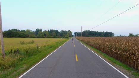 aerial view of young man on bike ride in country down a road in 4k