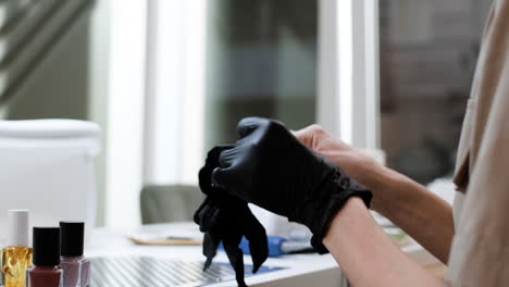 woman putting on black gloves in a nail salon