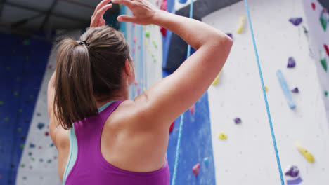 rear view of caucasian woman preparing to climb a wall at indoor climbing wall