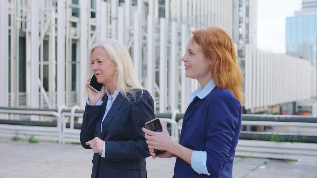 Two businesswomen using mobile devices in an urban setting