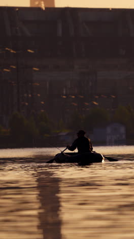 old man in inflatable boat sailing in the evening. fisherman in a rowboat with two oars on the background of a big plant. man tries to find a good place for fishing in the river. vertical video