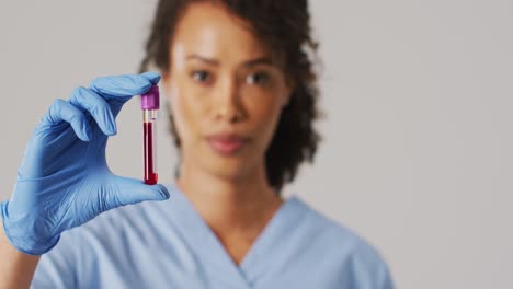 video de una doctora biracial sosteniendo un tubo de ensayo sobre un fondo azul