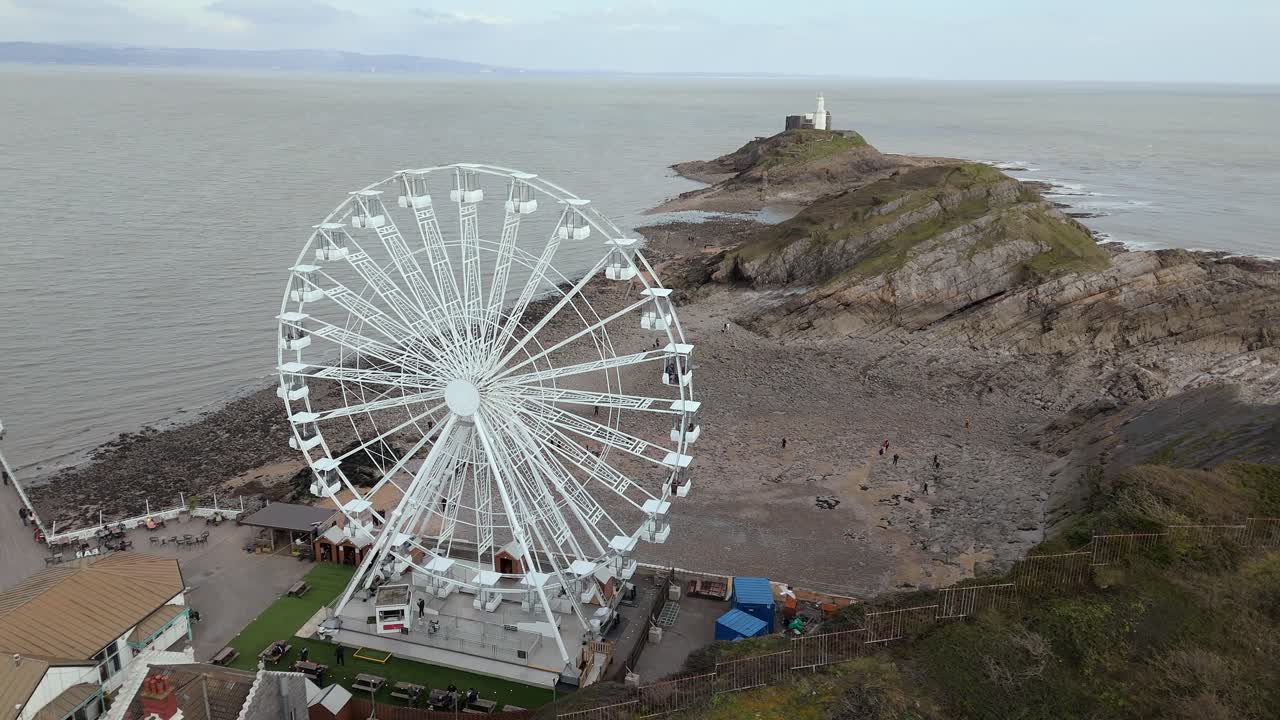 Drone shot of The Big Wheel rotating with tourists boarded and hazy seascape in England.