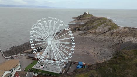 drone shot of the big wheel rotating with tourists boarded and hazy seascape in england.