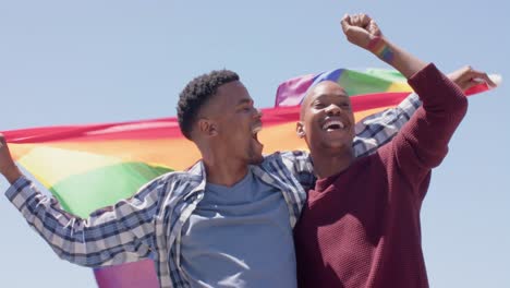 happy african american gay male couple holding lgbt rainbow flag, slow motion