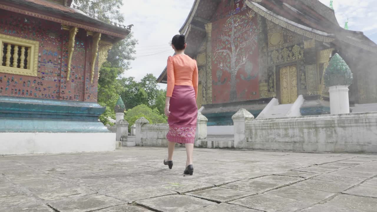 Back Of Asian Girl Wearing Traditional Dress Walk Around Xieng Thong Temple, Slow Motion