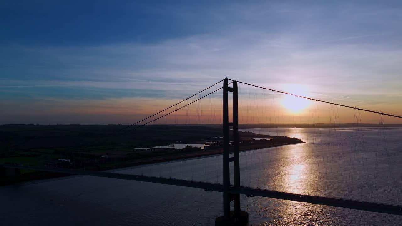 A visual symphony unfolds as Humber Bridge, drenched in the golden hues of sunset, frames the graceful passage of cars