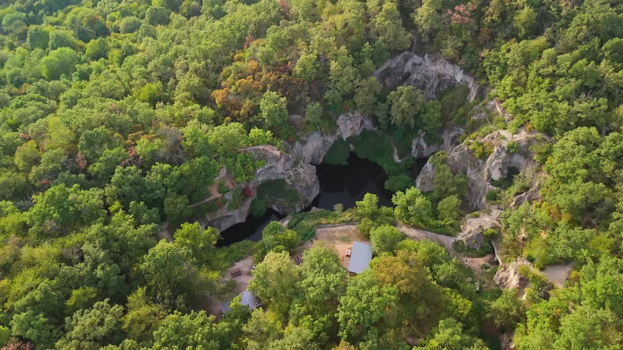 Orbiting aerial view of the Tarn of Megyer-hegy near Sárospatak, Hungary, showcasing lush greenery, rocky formations, and tranquil waters in a stunning millstone quarry turned nature preserve