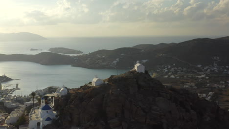 Sunset-drone-footage-circling-churches-on-the-hill-in-Chora-town-with-view-of-sea,-in-Ios,-Greece