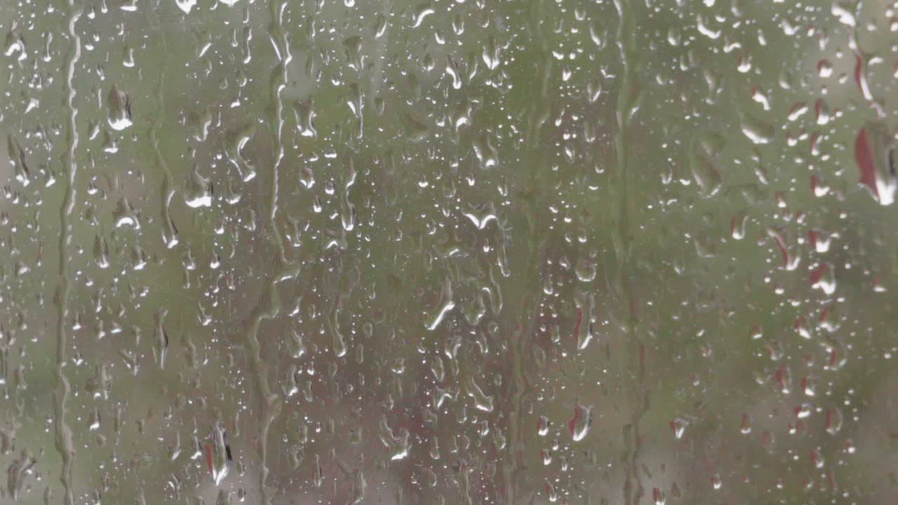 흐릿한 녹색 배경을 가진 창에 비 줄무늬와 물방울