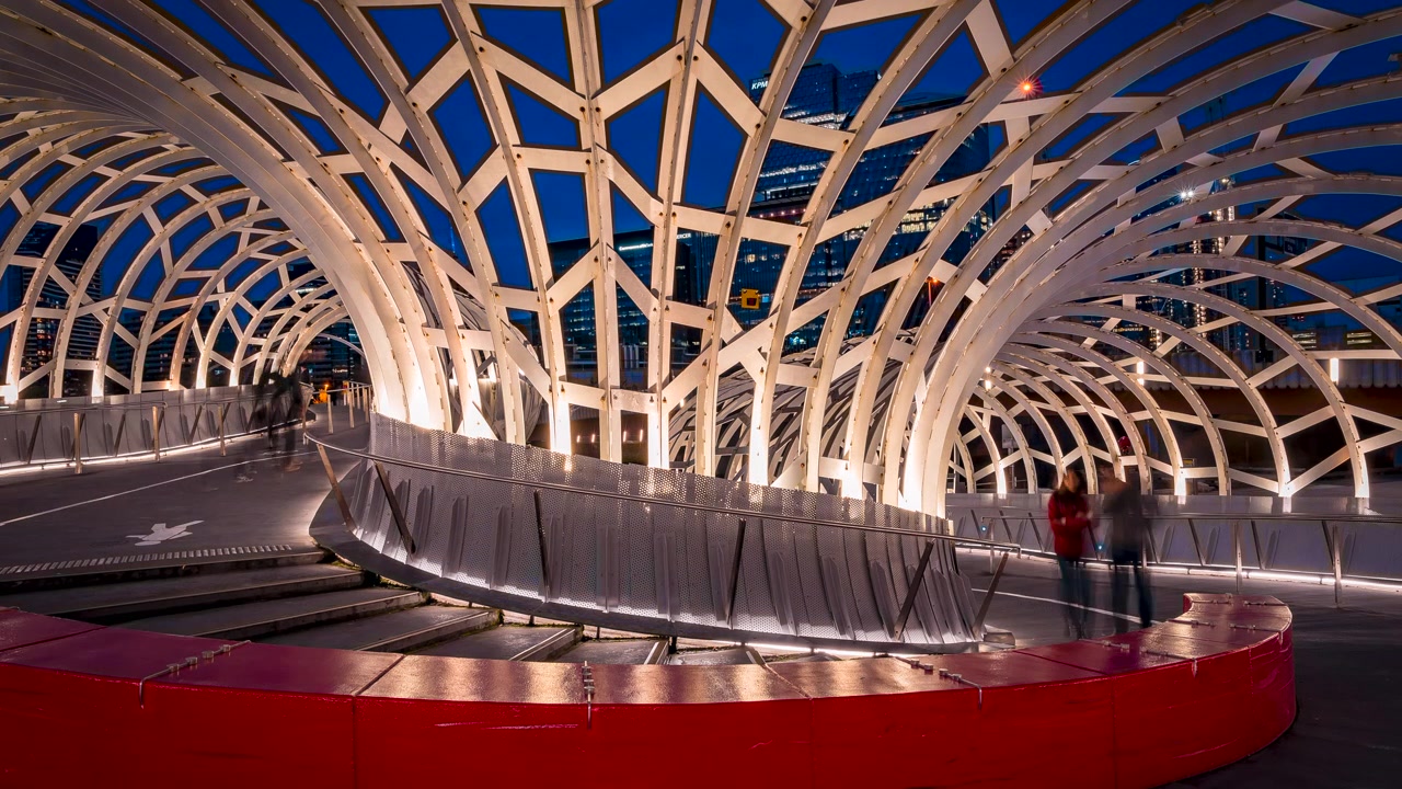 Timelapse inside Webb Bridge at Docklands, Melbourne, Australia, showcasing the illuminated steel architecture, geometric design and modern city skyline at blue hour.