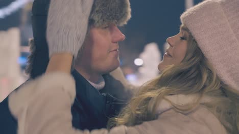 young-woman-hugs-guy-near-decorated-Christmas-tree-at-night