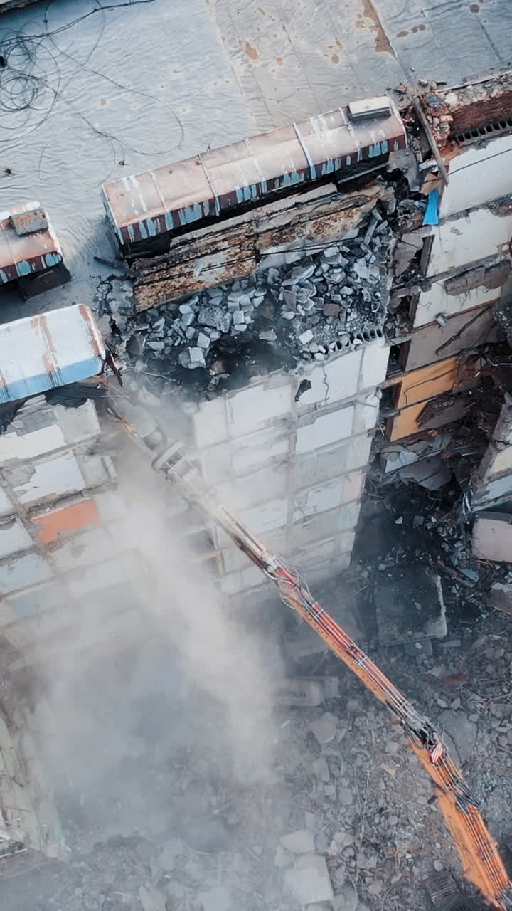 Destruction of an old multi-storey building by a machine. Work of the excavator at the construction site. A cloud of dust from destruction. Vertical video