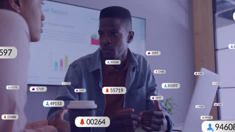 Animation-Von-Social-Media-Symbolen-Mit-Zahlen-über-Verschiedenen-Kollegen,-Die-Im-Büro-über-Die-Arbeit-Diskutieren