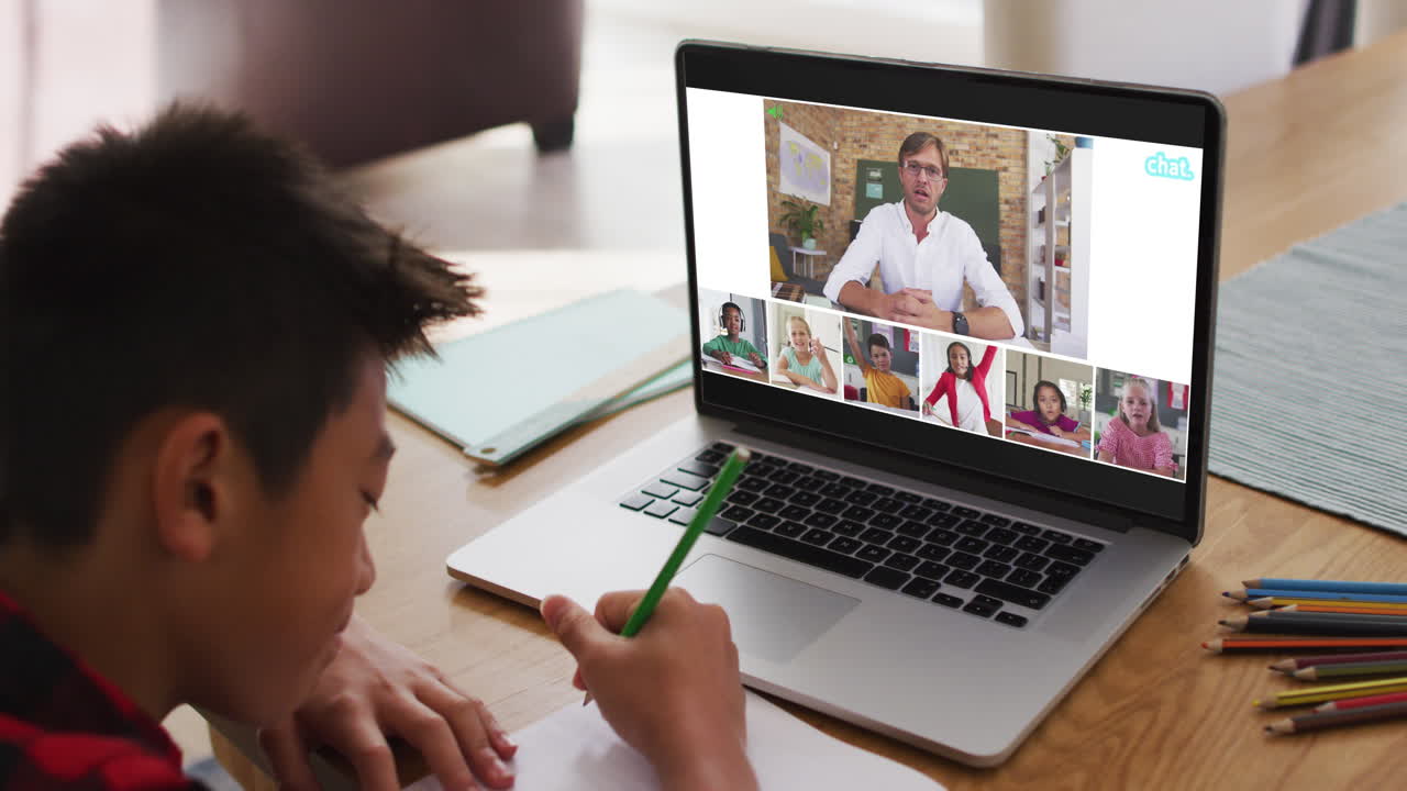 Schoolboy using laptop for online lesson at home, with diverse teacher and class on screen