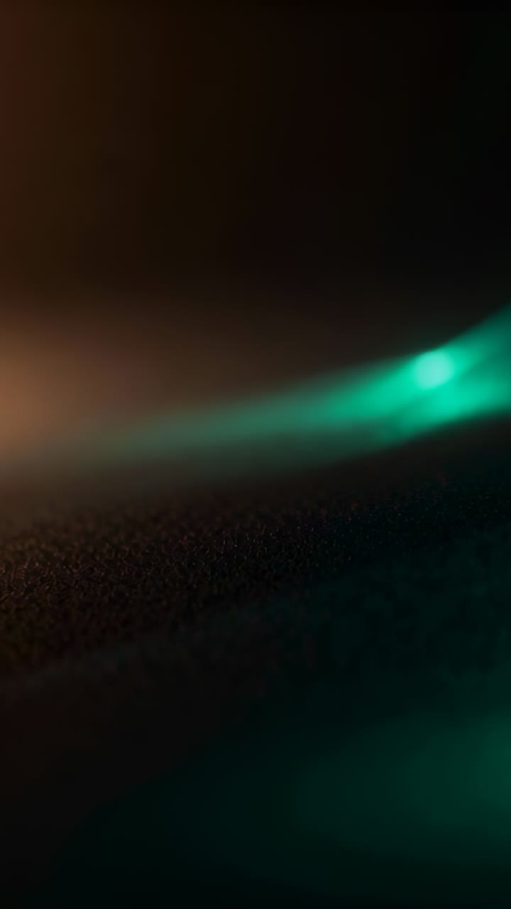 Vertical video: Shifting frames causing teal streak glowing, specks emerging on sand by orange glow