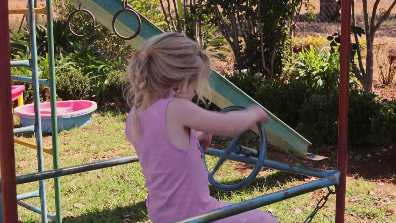Happy girl turns steering wheel in toy car on playground in summer