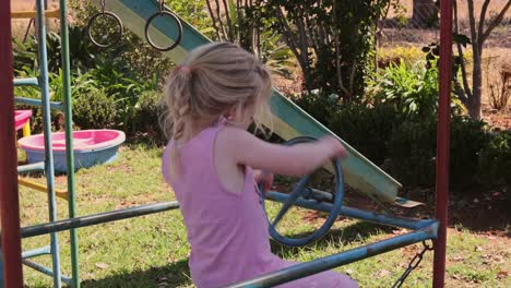happy girl turns steering wheel in toy car on playground in summer