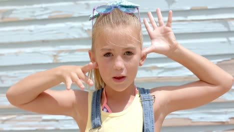 portrait of happy caucasian girl doing faces with hands over beach house