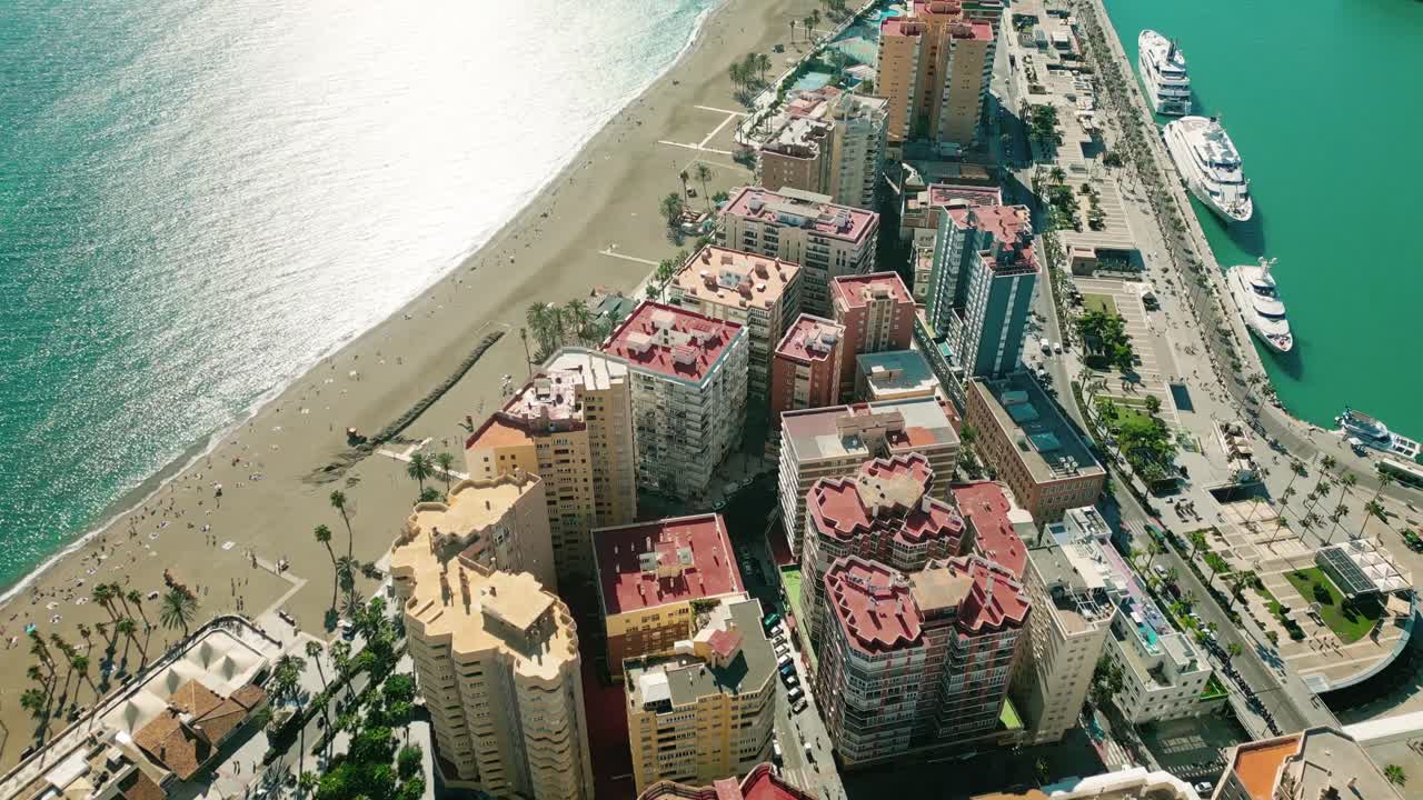 Drone soaring over vibrant sunlit coastline of Málaga, highlighting luxurious residences, Malagueta beach with its turquoise sea, and yachs parked along the port