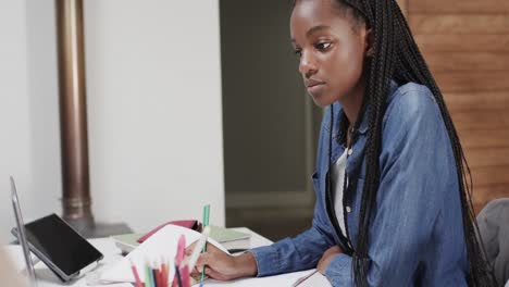 une adolescente afro-américaine concentrée étudie à la maison en utilisant un ordinateur portable à la table à manger