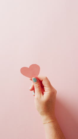 vertical video of caucasian woman's hand holding pink heart on pink background with copy space